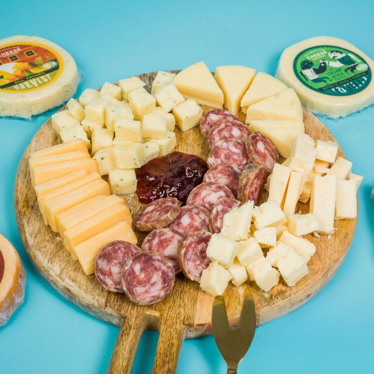 Wooden board with assorted cheeses and sausages on a blue background