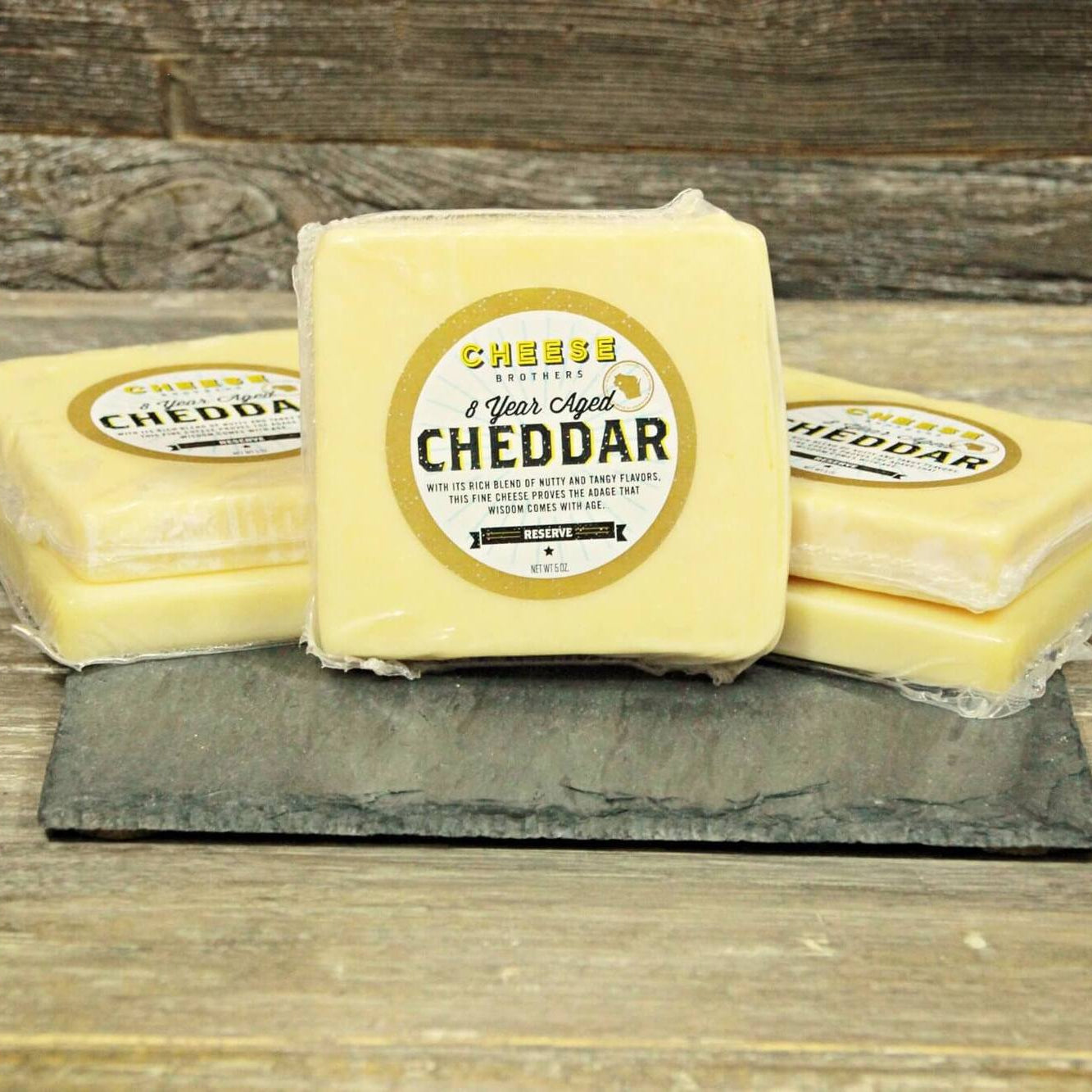 Three blocks of cheddar cheese with labels on a wooden surface