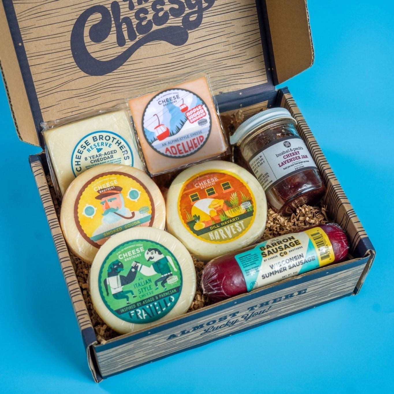 Box of assorted cheeses and condiments with visible branding on a blue background