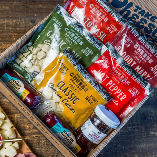 Assorted snack items including cheese puffs, chips, and dips in a box on a wooden surface.