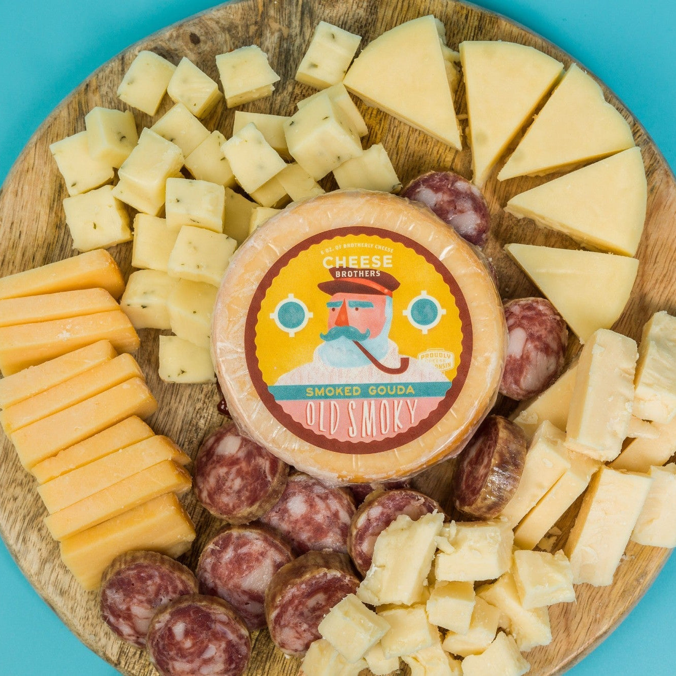Wooden cheese board with various types of cheese and a round cheese wheel on a blue background.