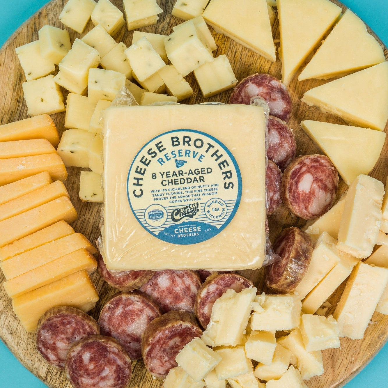 Assorted cheeses and sausages on a wooden board with Cheese Brothers Reserve Cheddar block.